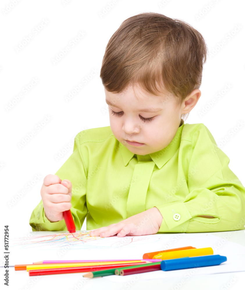Little boy is drawing on white paper using crayon Little boy is drawing on white paper using crayon