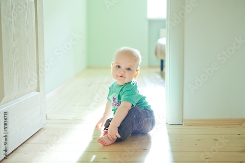 Chubby baby boy sitting on wooden floor at home