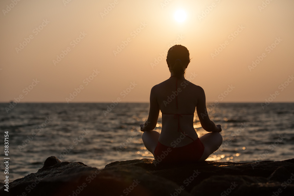 Silhouette of woman that meditates at the sea during sunset