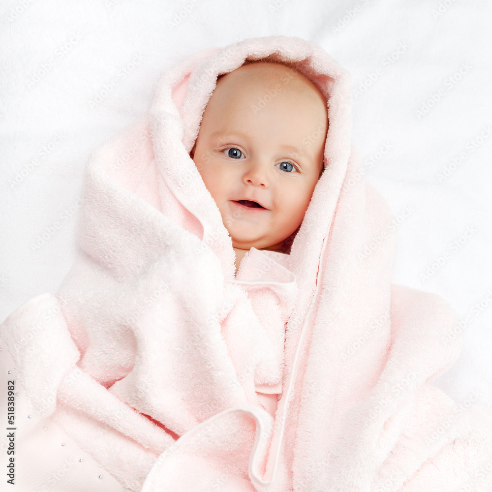 Caucasian baby boy covered with pink towel joyfully smiles at ca Caucasian baby boy covered with pink towel joyfully smiles at ca