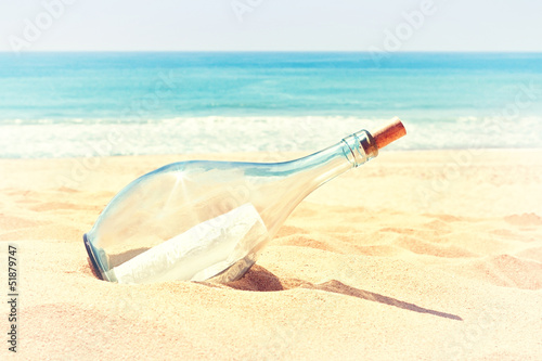 A bottle with a letter of distress in the sand on the beach. In