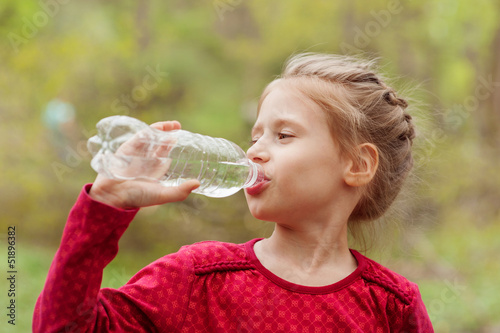 Girl drinks water from a bottle in a park