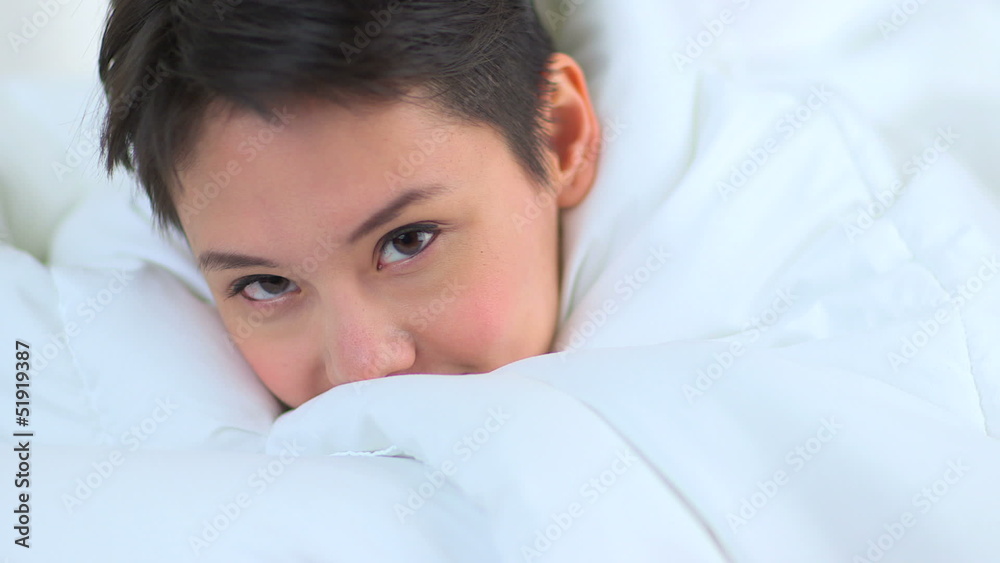 Mixed race Asian woman smiling under sheets in bed Mixed race Asian woman smiling under sheets in bed