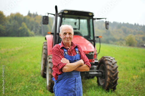 Tableau sur toile Fier fermier debout devant son tracteur rouge