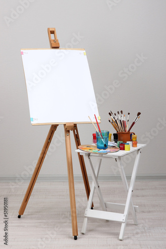 Wooden easel with clean whatman paper and art supplies in room