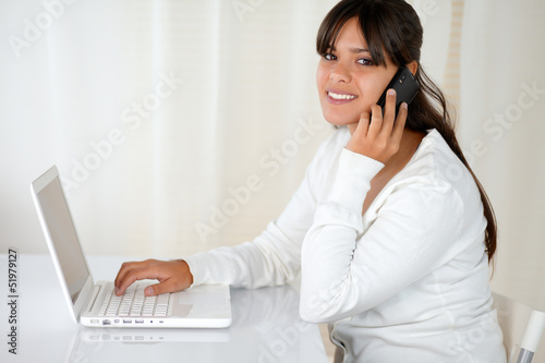 Latin woman using her laptop speaking on cellphone