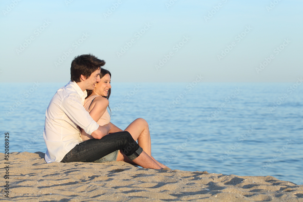 Couple cuddling sitting on the sand of the beach