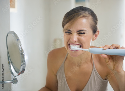 Young woman brushing teeth with grimace on face photo