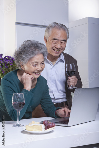 Mature Couple Looking at Laptop in the Kitchen, Drinking Wine 