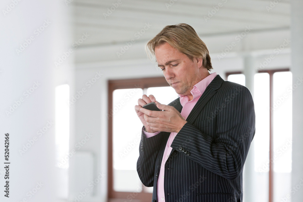 Business man with blonde hair using cellphone in white office. Business man with blonde hair using cellphone in white office.
