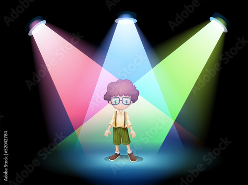 A boy wearing an eyeglass standing on the stage with spotlights