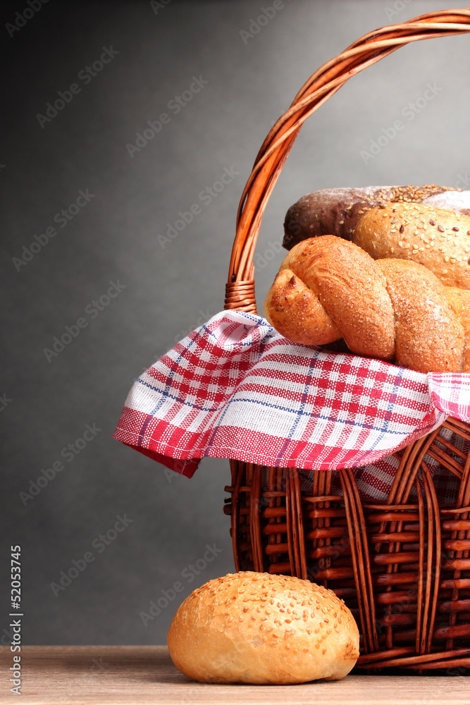 delicious bread in basket on wooden table on gray background