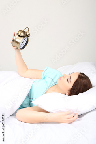 Beautiful young woman on bed with alarm clock in bedroom