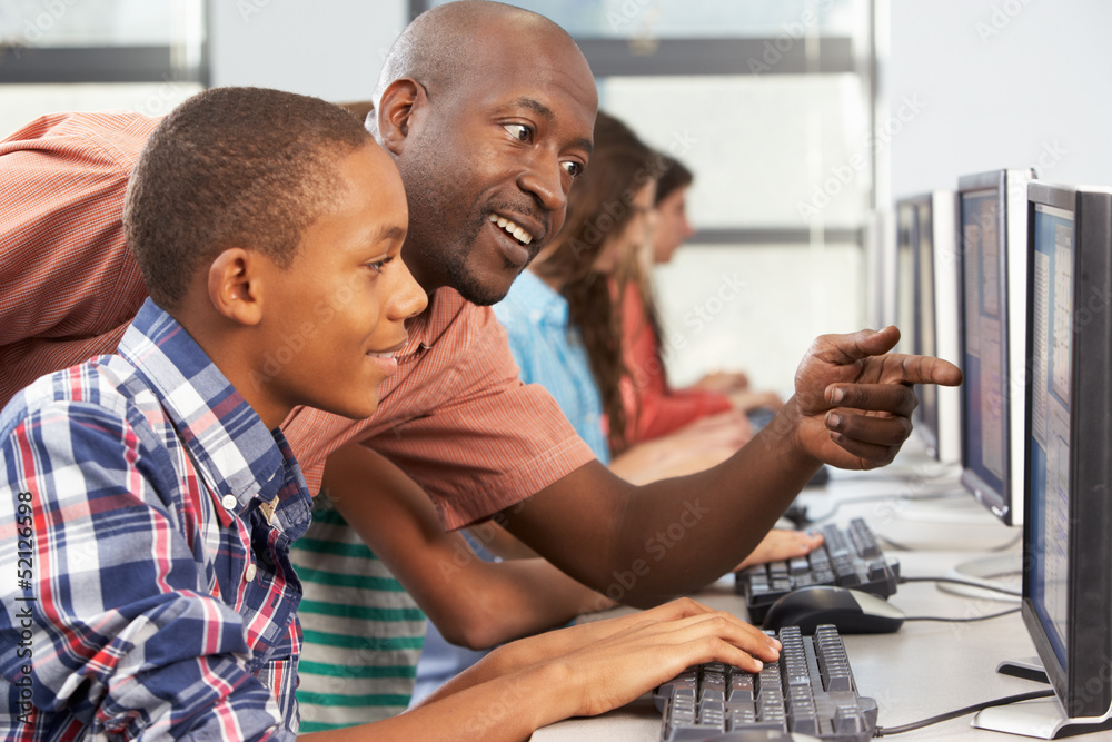 Obraz premium Teacher Helping Students Working At Computers In Classroom