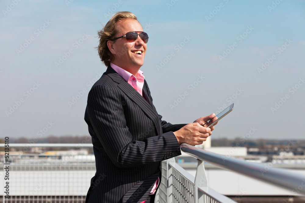 Business man with sunglasses outdoor on rooftop using tablet.