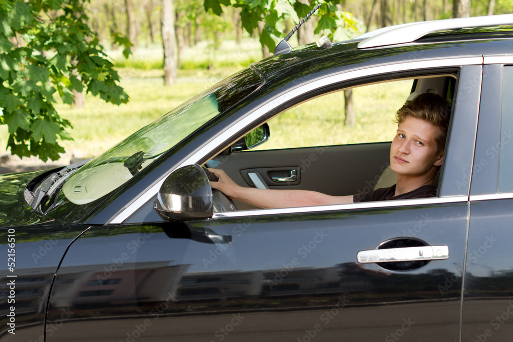 Cute young boy driving a black car and posing