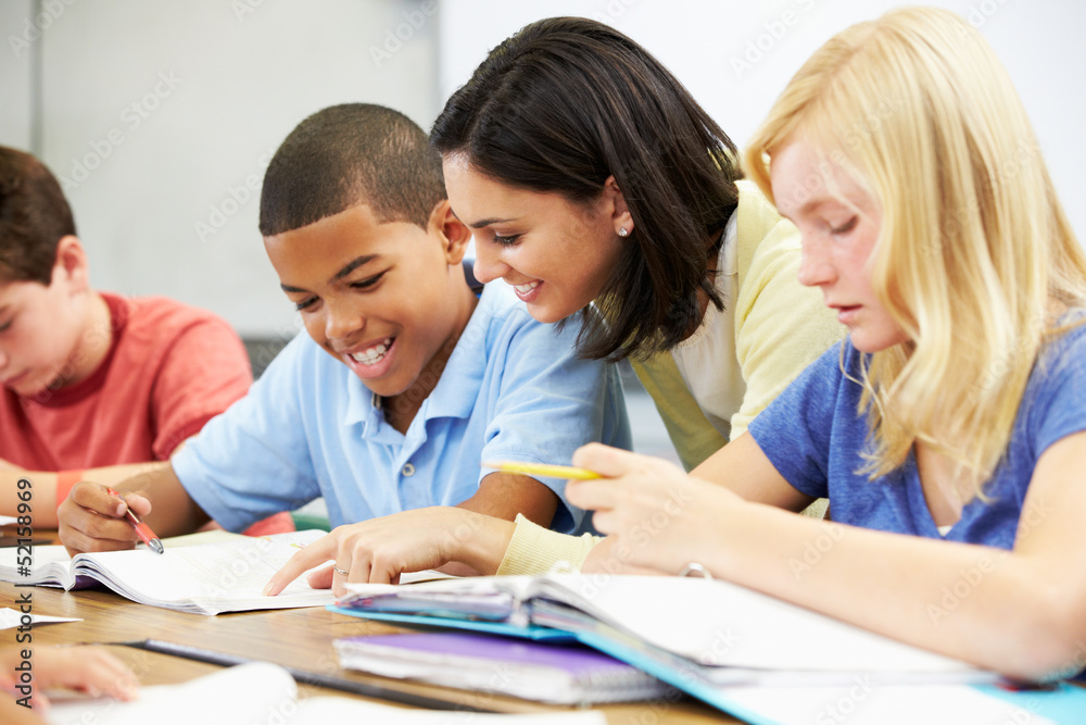 Teacher Helping Pupils Studying At Desks In Classroom Teacher Helping Pupils Studying At Desks In Classroom