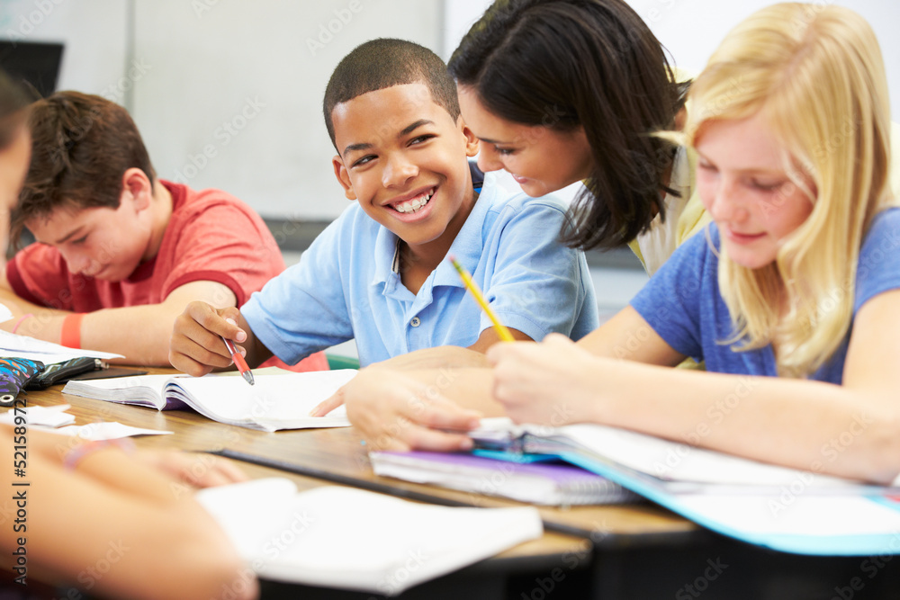 Teacher Helping Pupils Studying At Desks In Classroom Teacher Helping Pupils Studying At Desks In Classroom