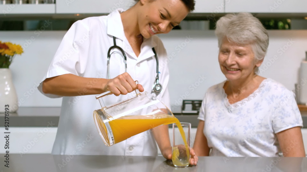Home help pouring orange juice for patient in kitchen
