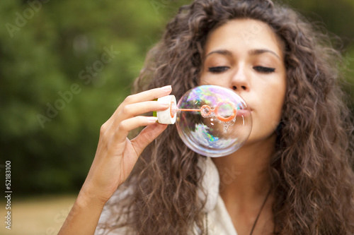 Beautiful hippie girl in the park blowing bubbles
