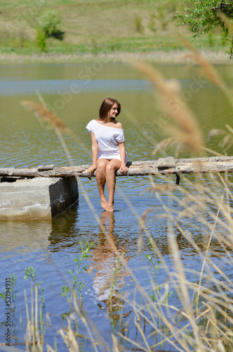 Fototapeta Naklejka Na Ścianę i Meble -  Happy young woman in white dress sitting on pier