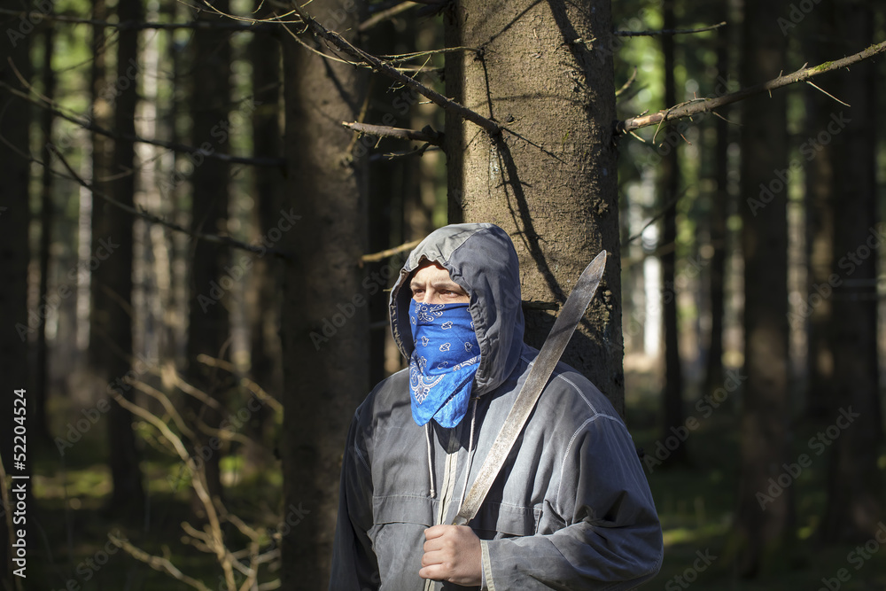 Man with a machete in the woods leaning against tree