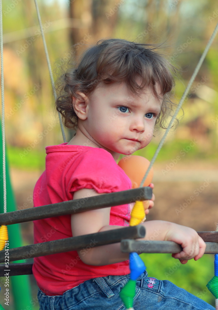 Cute child girl swinging and looking serious on summer backgroun Cute child girl swinging and looking serious on summer backgroun