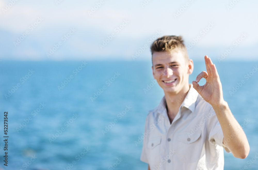 Smiling boy showing okay sign on sea background