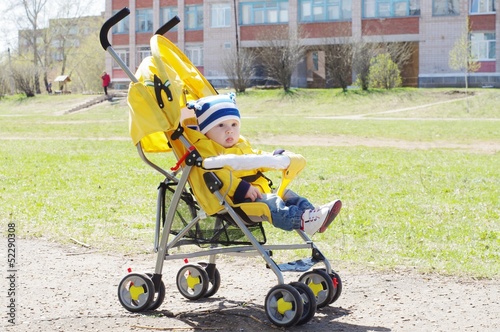 baby age of 7 months outdoors on yellow baby carriage in spring