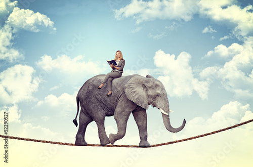 caucasian businesswoman gets carried away by a big elephant walking on a rope. concept of security and trust.