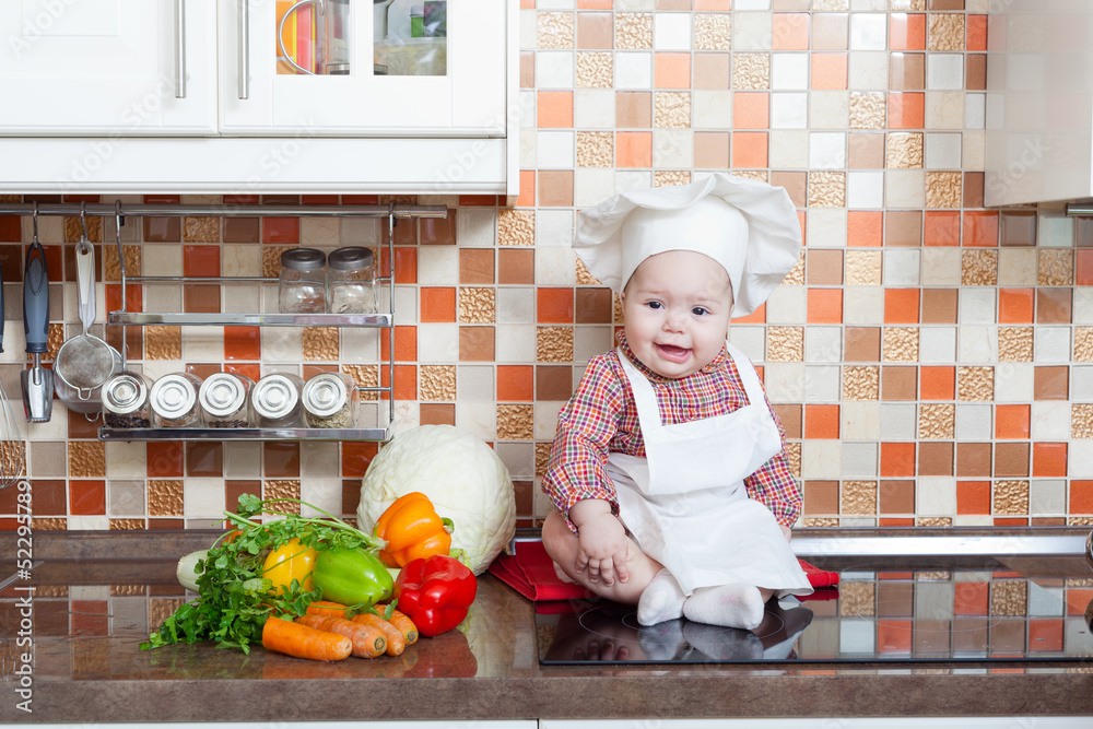 Baby cook with vegetables sits on a kitchen table Baby cook with vegetables sits on a kitchen table