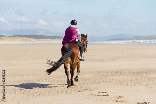 Lady riding down the beach on her horse. 