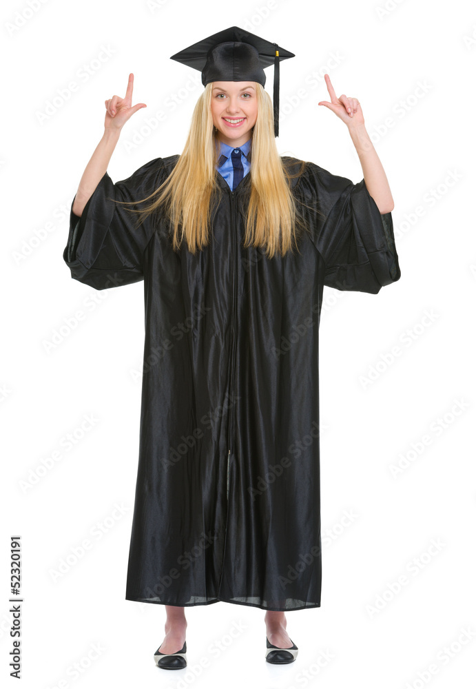 Happy young woman in graduation gown pointing up Happy young woman in graduation gown pointing up