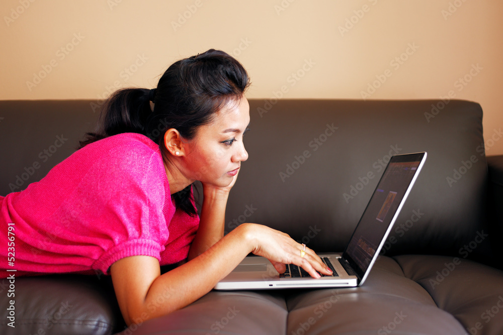Young woman in a pink top laying on a couch and using a laptop