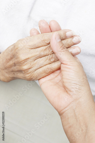 Hand of a younger woman holding the hand of an elderly woman.