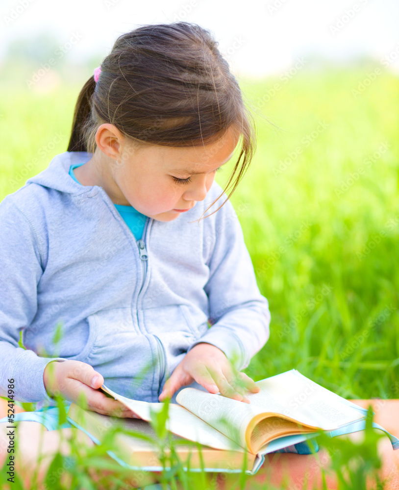 Little girl is reading a book outdoors Little girl is reading a book outdoors