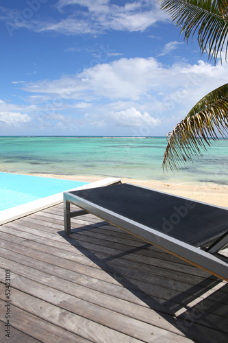 Infinity pool with deck chair by the beach © goodluz