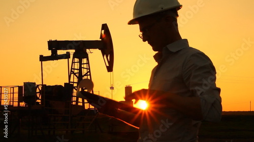 Man (engineer) with securities for the oil pumping unit. sunset 