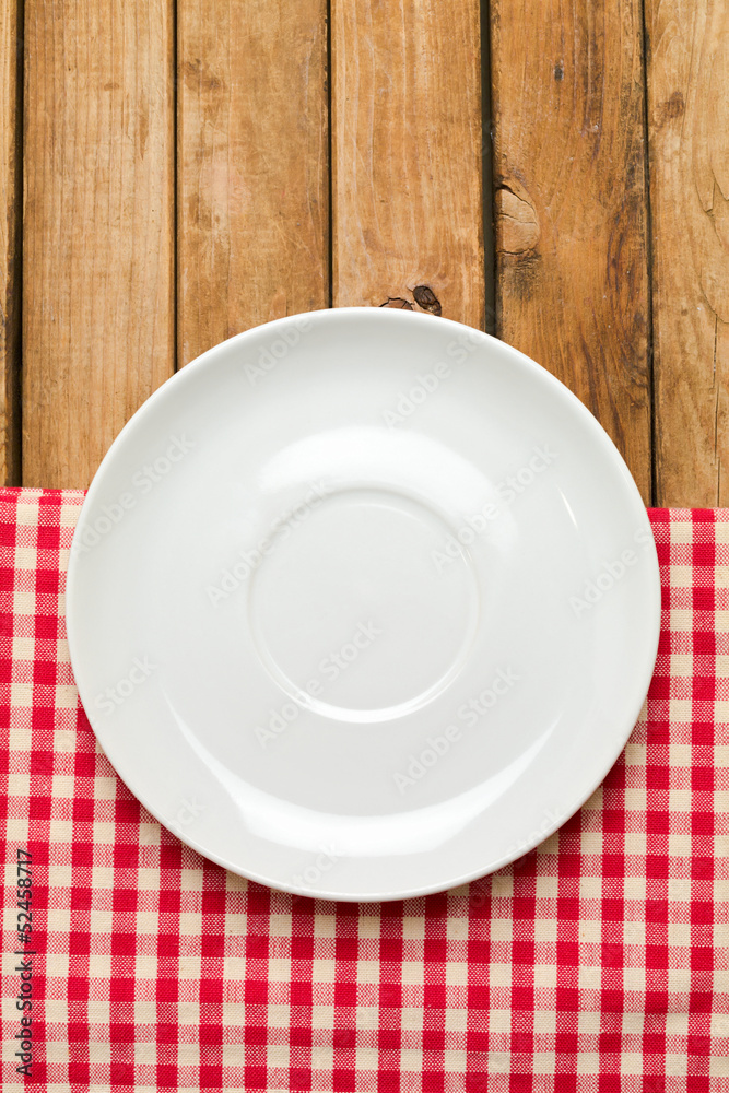 Empty plate on tablecloth over wooden background Empty plate on tablecloth over wooden background