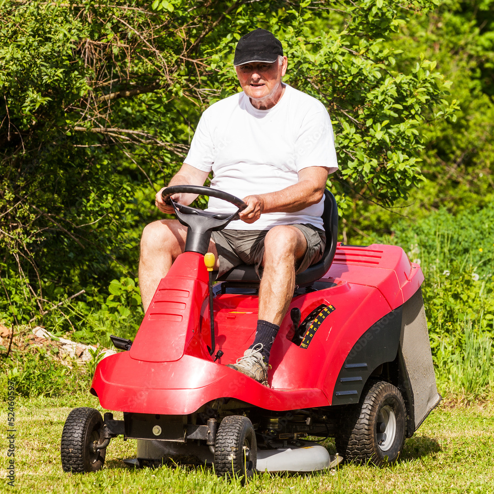 Fototapeta premium Senior man driving a red lawn mower (tractor)