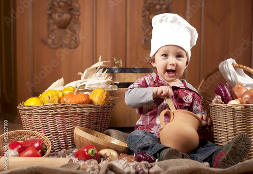 boy in a cook cap among pans and vegetables in kitchen
