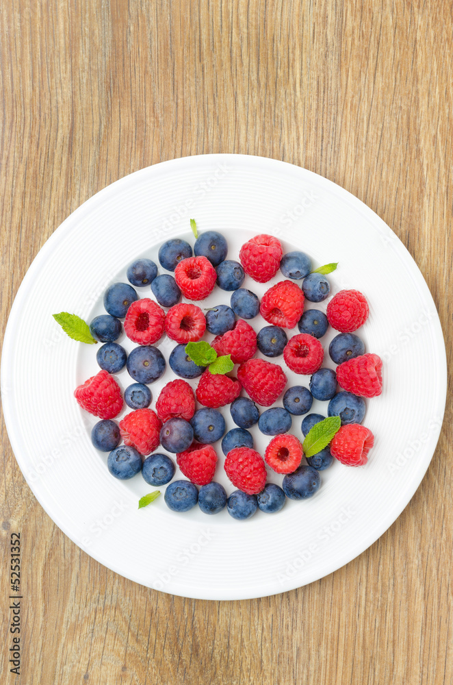 Fresh raspberries and blueberries on a plate on a wooden table Fresh raspberries and blueberries on a plate on a wooden table
