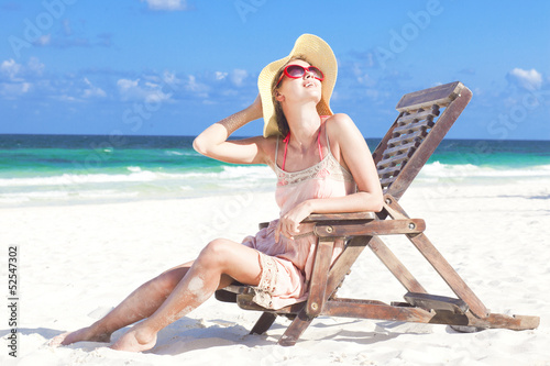 young woman in straw hat and bikini sitting on beach chair