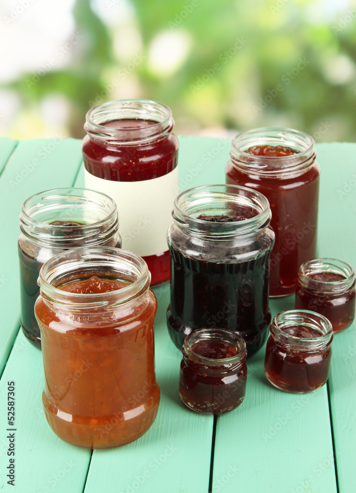 Tasty jam in banks on table on bright background