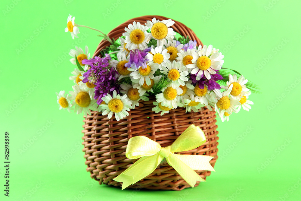 Naklejka premium Beautiful wild flowers in basket, on green background