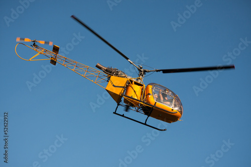 Flying yellow helicopter on blue sky