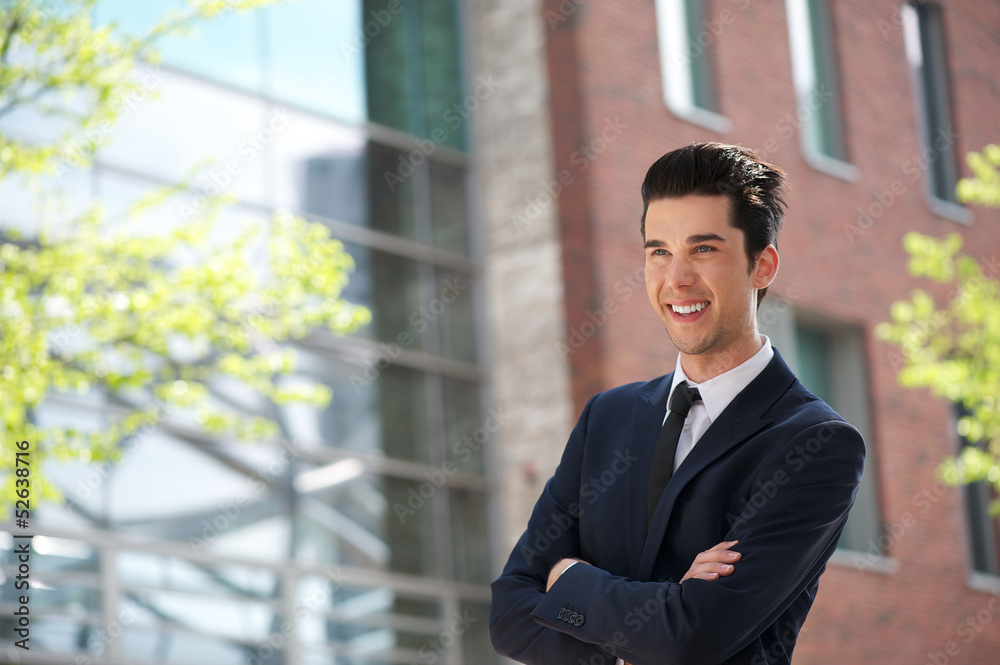 Smiling businessman standing outdoors with arms crossed