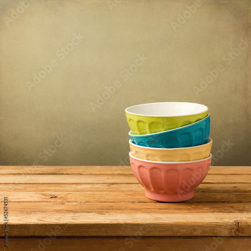 Colorful bowls on wooden table over grunge background