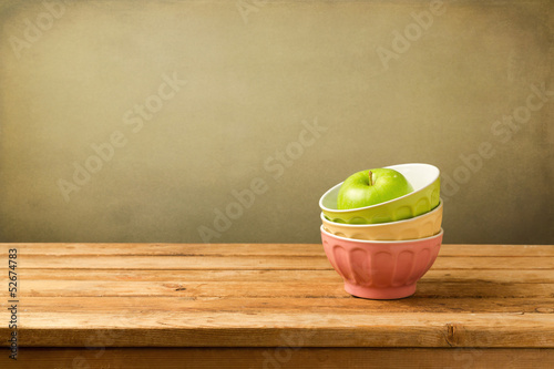 Colorful bowls with apple on wooden table