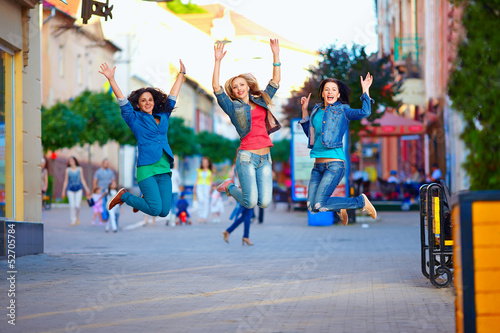three happy girls jumping on crowded city street